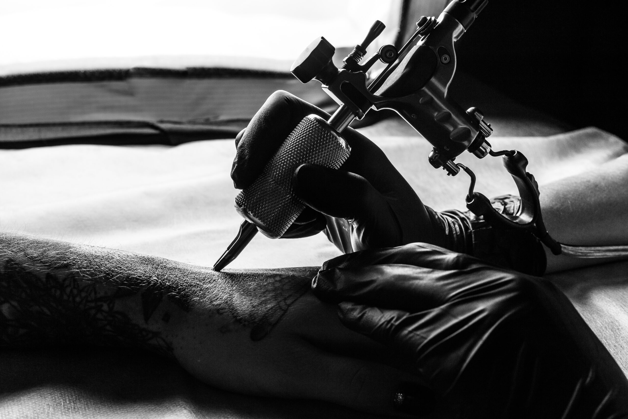 Close up picture of tattooist make a tattoo on clients arm in bw. Master works on the desk in black sterile gloves and hold a tattoo machine.